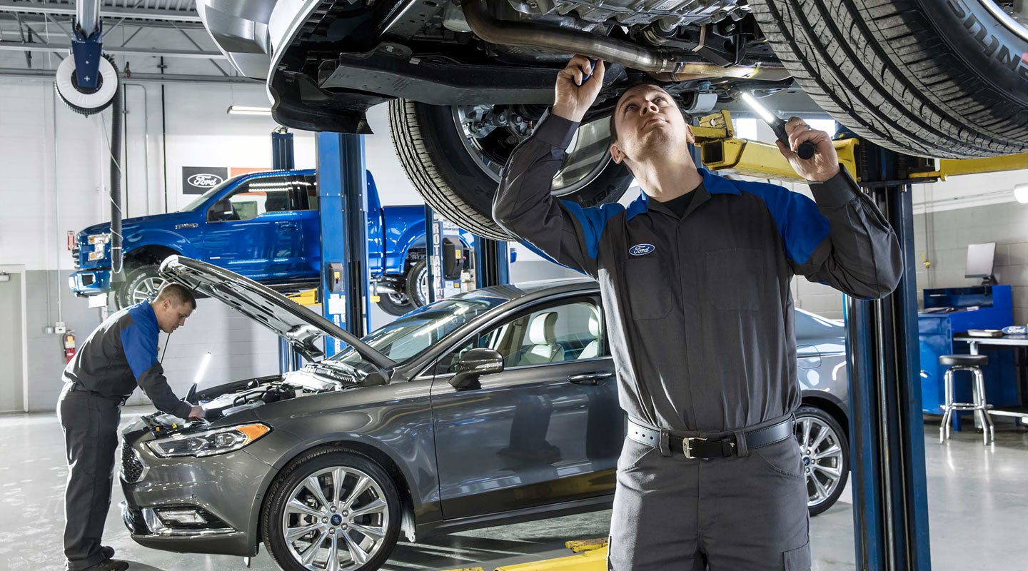 Smiling technician servicing a car engine while holding a tablet.