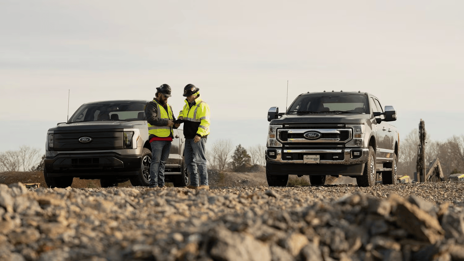 2 people discussing something on site with 2 ford car standing near