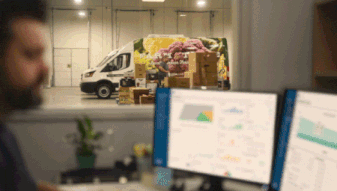 Warehouse worker at desk monitoring deliveries as van unloads packages