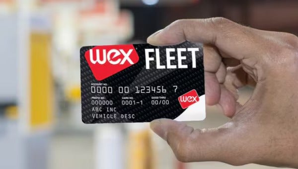 Hand holding a WEX Fleet fuel card at a gas station