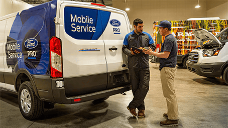 Two men talking beside a Ford Mobile Service van inside a garage