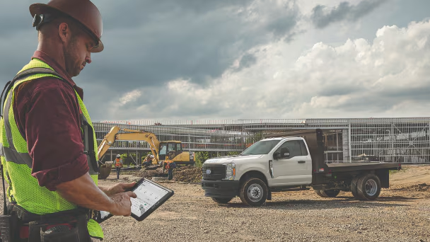 Man analyzing data on tablet at construction site with Ford truck nearby.