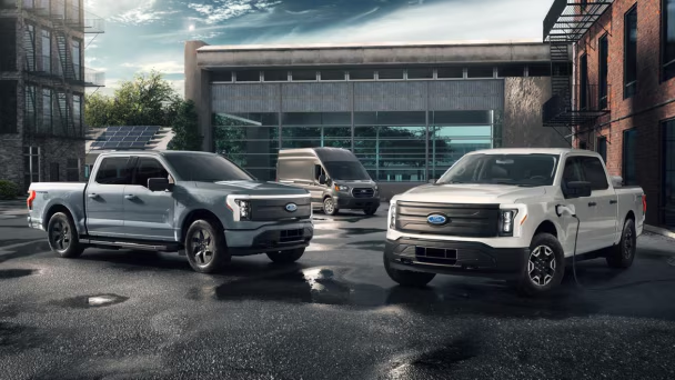 Electric Ford trucks and van parked in urban charging zone.