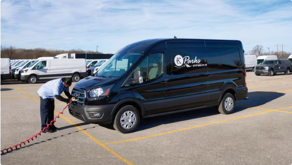Worker charging black Parks service van in parking lot.