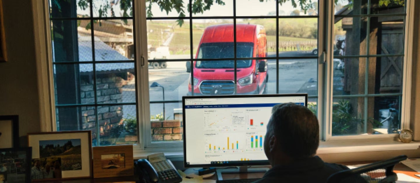 Businessman tracking delivery data as red van arrives outside office window